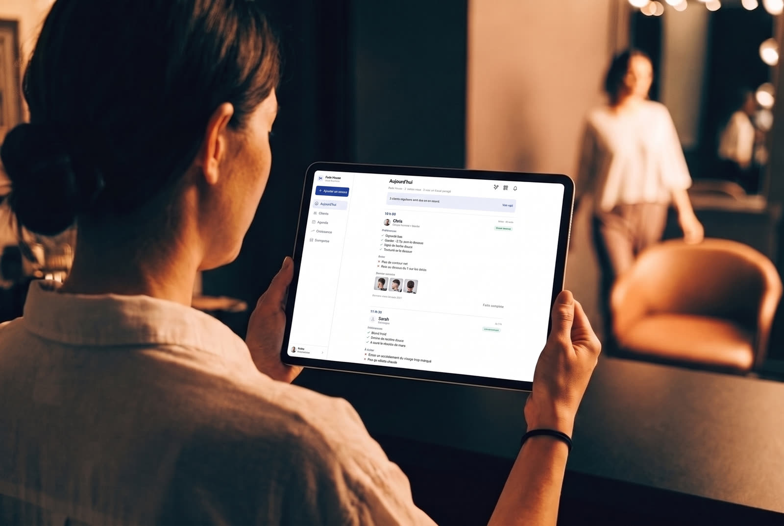 Une propriétaire de commerce tient un iPad affichant la vue Aujourd’hui de Usual Business, pendant qu’une cliente entre derrière elle.