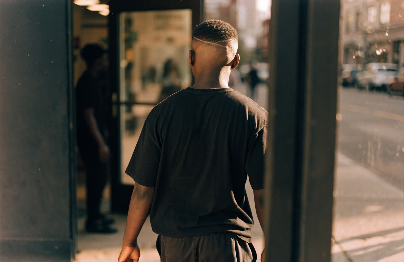 A client stepping out of a barbershop onto a sunny street.