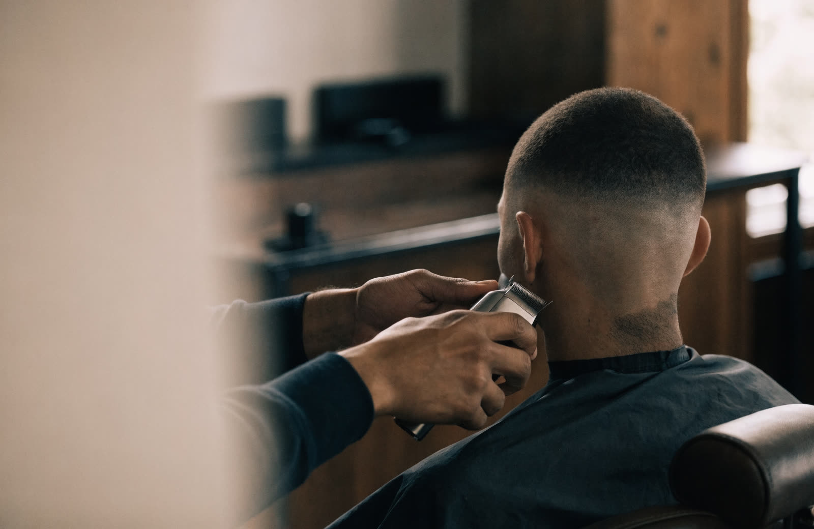 A barber working through a skin fade in a bright shop.