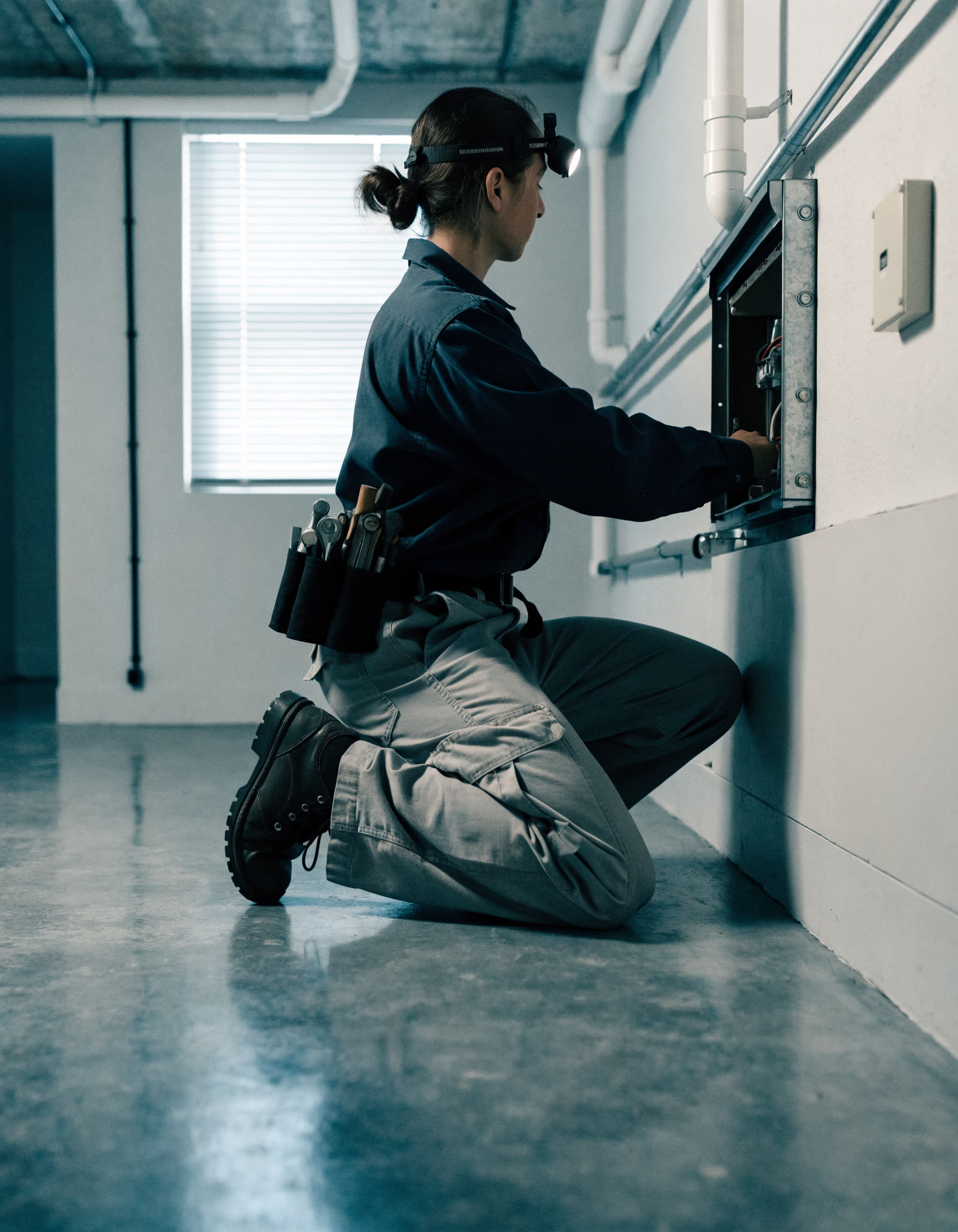 A technician kneeling to service a furnace in a basement.