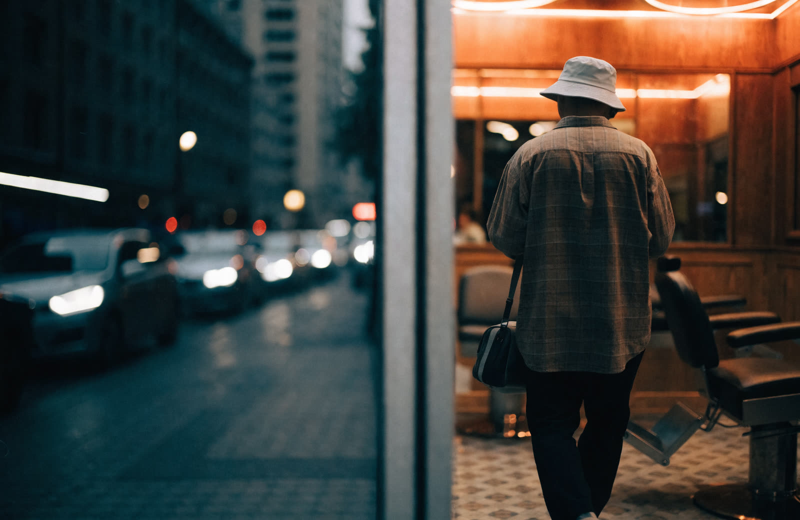 A traveller with a bag walking into a lit barbershop at night, in a city they do not know.